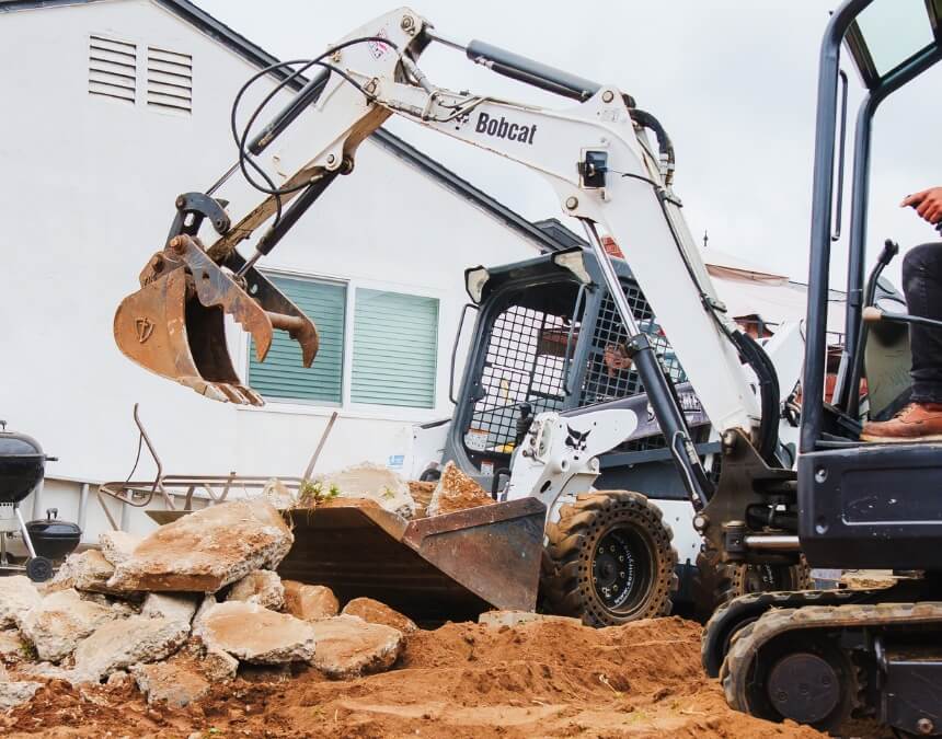 Bobcat excavator clearing broken concrete during garage ADU site prep