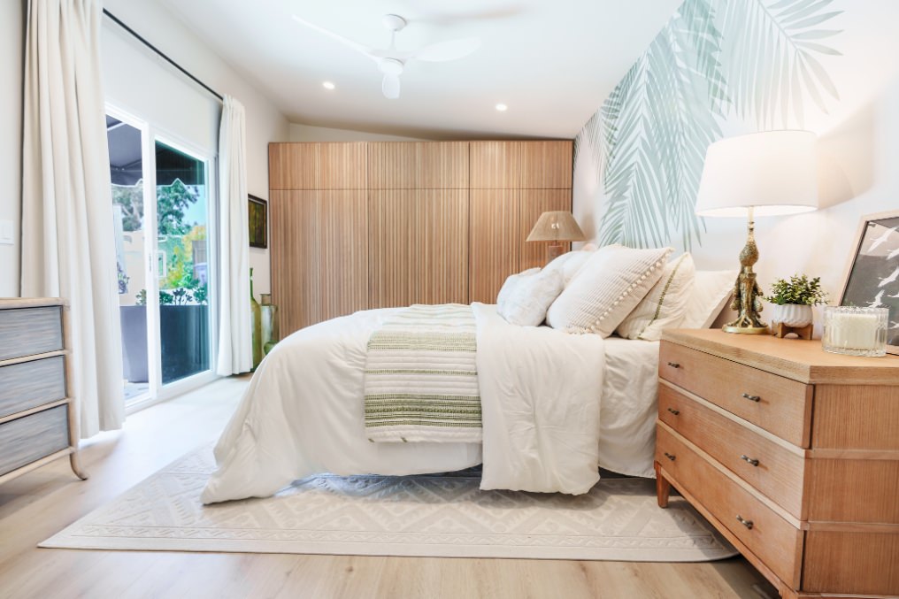 Peaceful boho-chic bedroom with palm leaf accent wall, natural wooden furniture, and sliding doors to patio