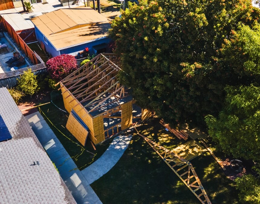Aerial view of backyard showing early framing stage of detached ADU construction near large tree canopy