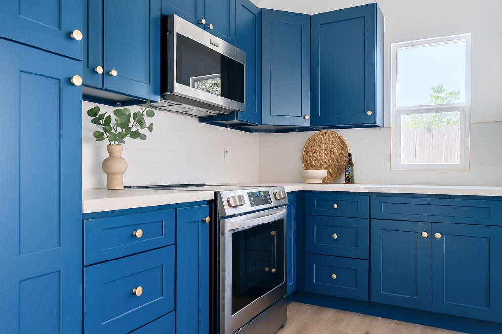 Close-up of stylish blue kitchen cabinetry accented with gold hardware and stainless steel appliances