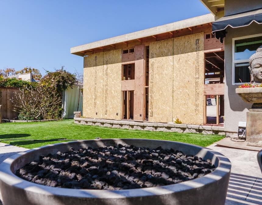 Backyard ADU under construction, with sheathing installed on framing and modern landscaping visible in the foreground.