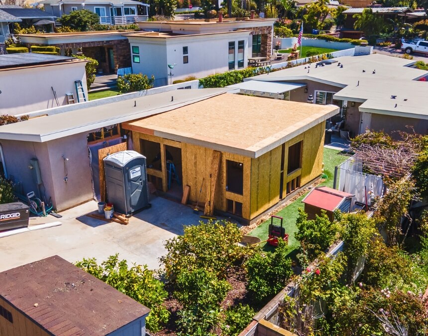 Aerial photo of an ADU mid-construction in a suburban California backyard with adjacent homes and visible roofing work