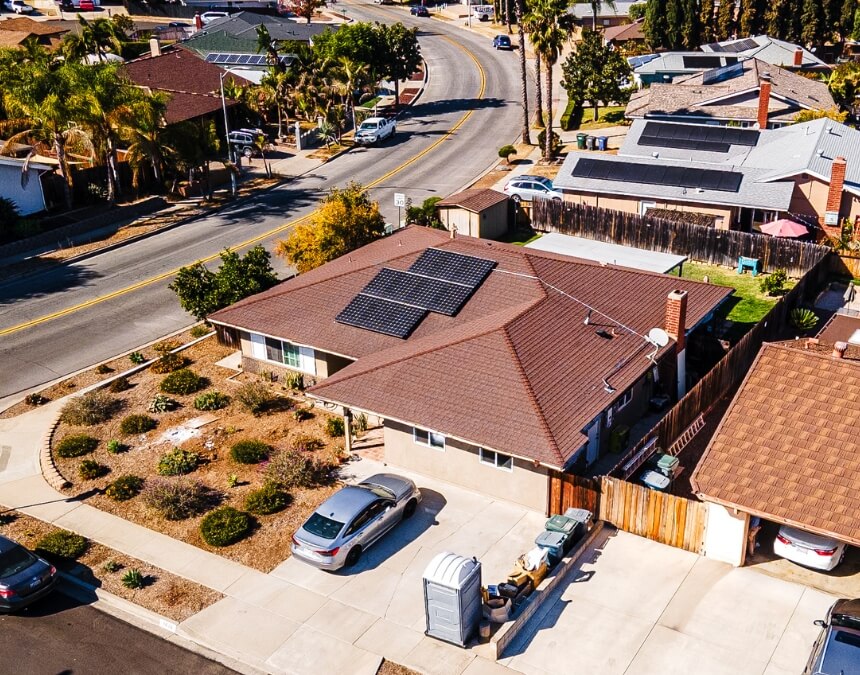 Aerial view of a modern San Diego home with black roof-mounted solar panels and an ADU construction site in front.