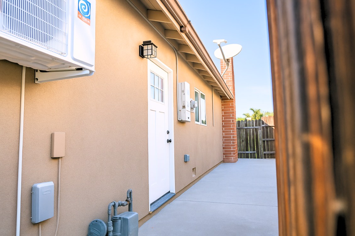 Side view of ADU with tan stucco exterior, white entry door, and utility hookups