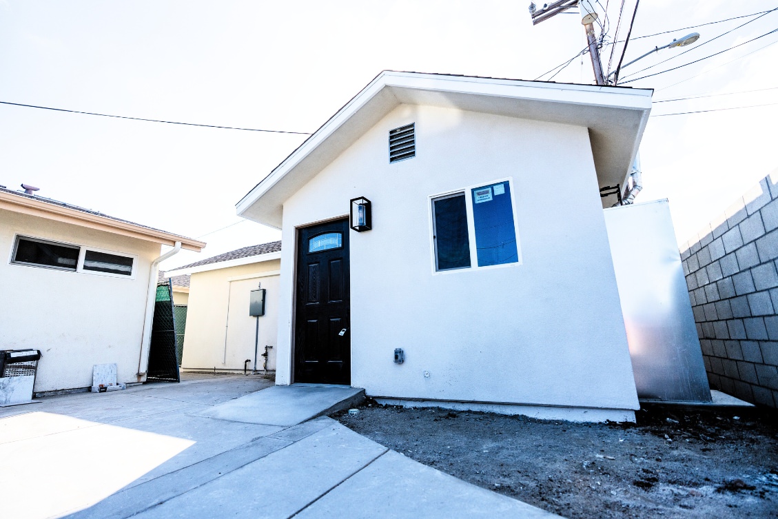 Compact detached ADU with white stucco exterior, dark front door, and paved driveway