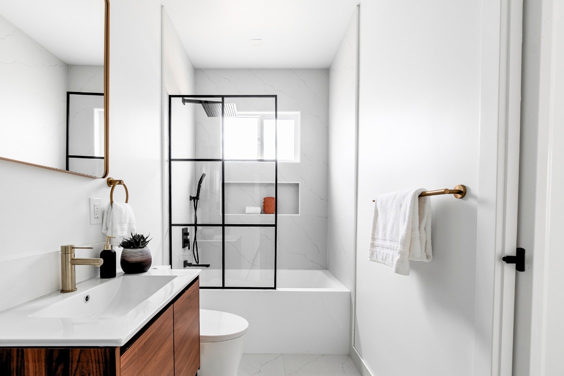 Modern ADU bathroom with black grid glass shower, floating wood vanity, and gold accents