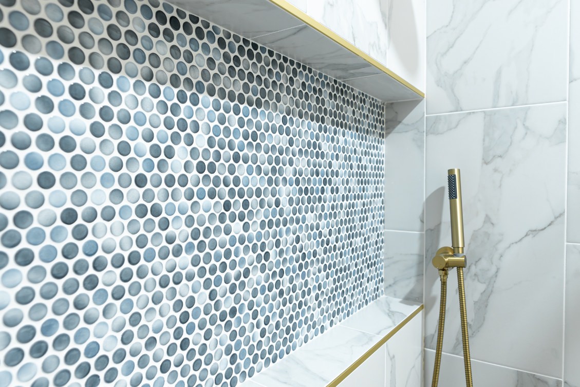 Close-up of ADU shower niche with blue penny tile accent and gold handheld showerhead