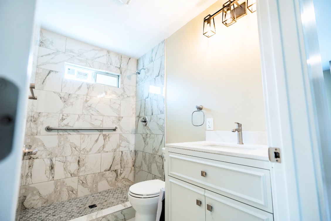 ADU bathroom with marble tile walk-in shower, grab bar, and white vanity