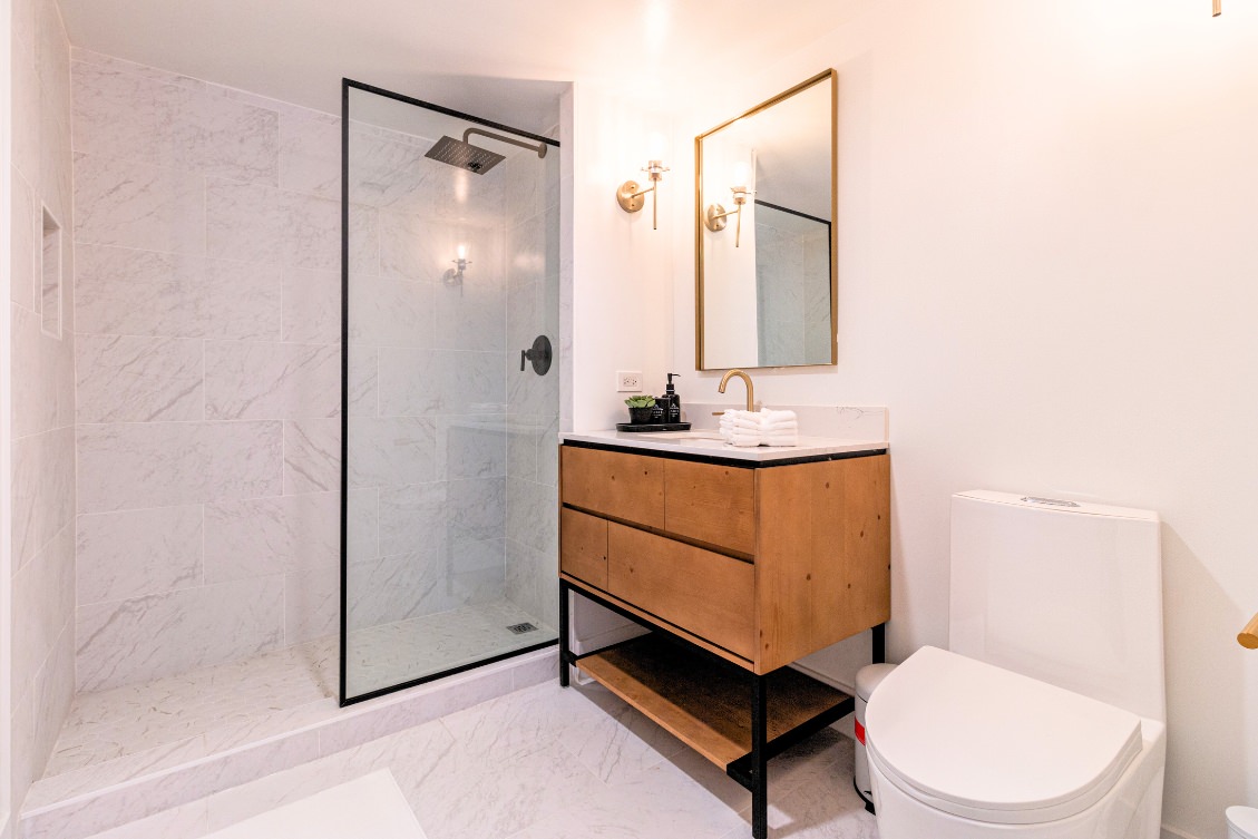 Modern ADU bathroom with wood vanity, glass shower enclosure, and gold fixtures