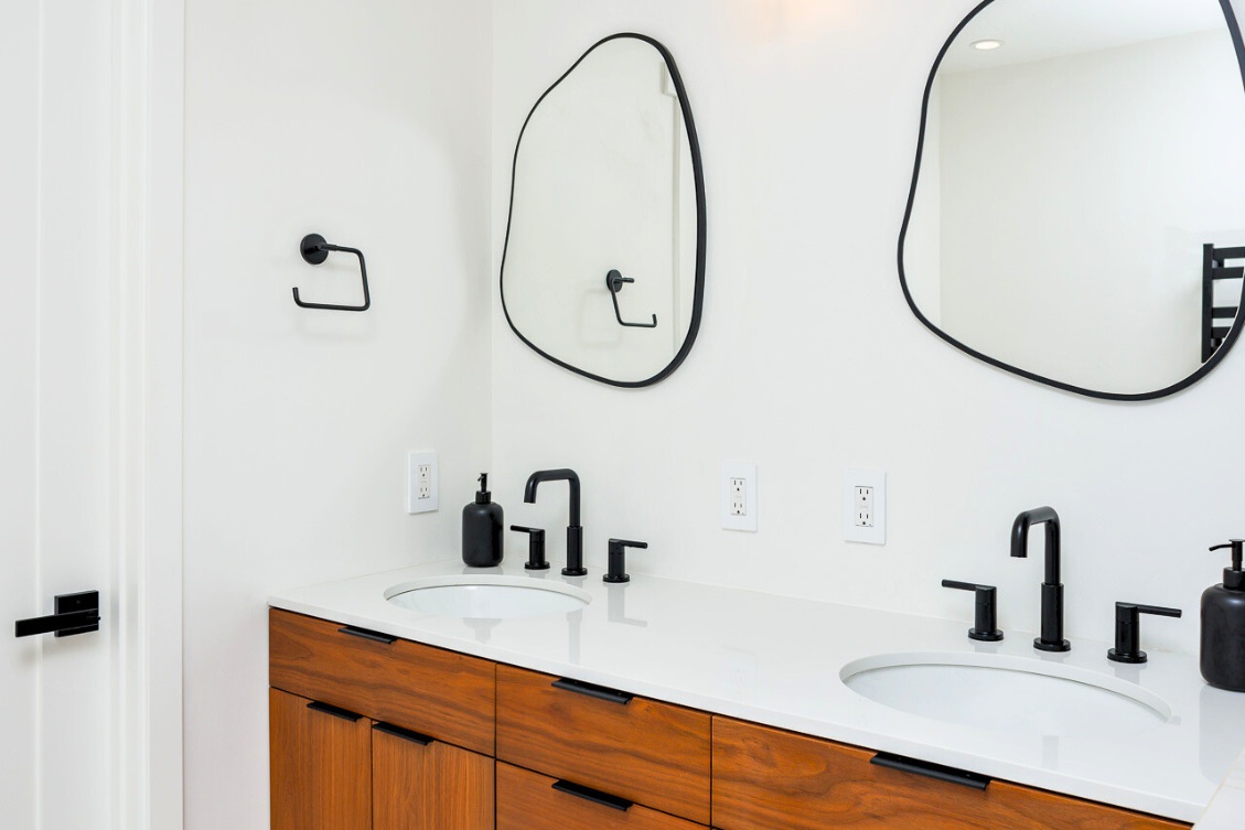 Double vanity ADU bathroom with wood cabinets, black faucets, and asymmetrical mirrors