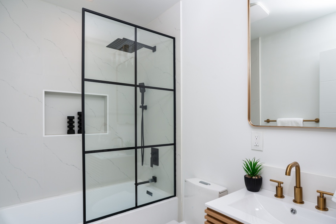 Contemporary ADU bathroom with tub-shower combo, black grid glass door, and gold faucet accents