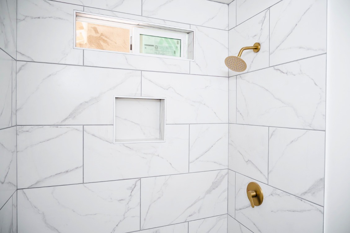 ADU shower detail with marble tile walls, niche shelving, and gold rain shower head