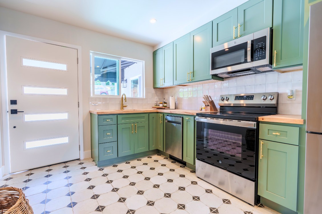 Compact ADU kitchen with green shaker cabinets, brass hardware, and stainless steel appliances