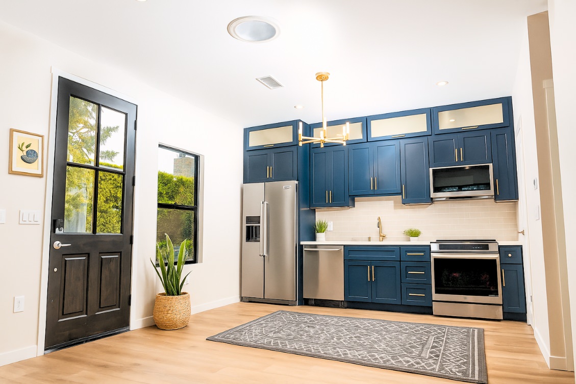 Contemporary ADU kitchen with navy cabinets, glass uppers, and gold chandelier lighting