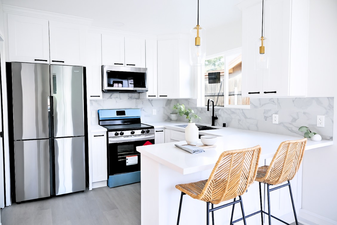Bright ADU kitchen with white cabinets, marble backsplash, and rattan barstools at peninsula