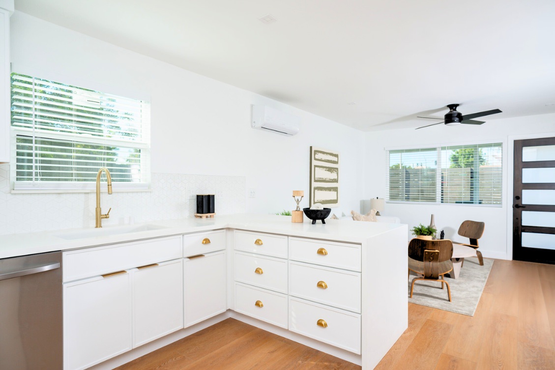 Minimalist ADU kitchen with white cabinetry, gold pulls, and open-concept layout into living room