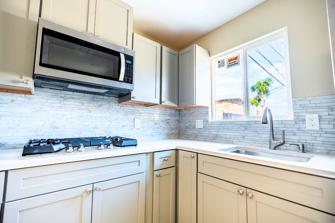 Compact ADU kitchen with light gray cabinets, marble tile backsplash, and stainless appliances