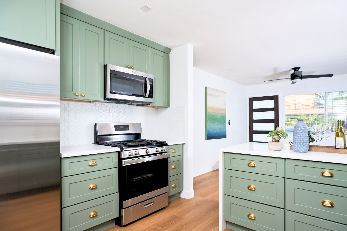Open ADU kitchen with green shaker cabinets, brass hardware, and kitchen island with storage
