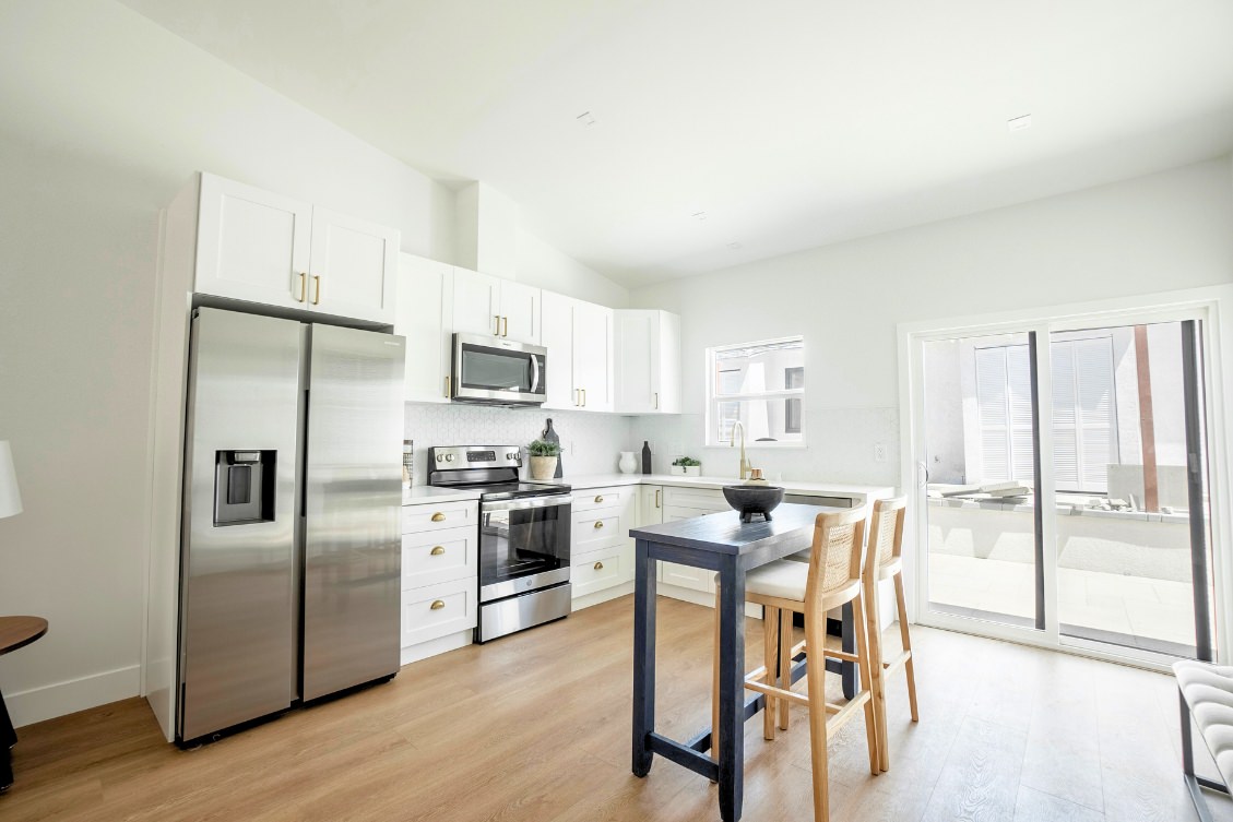 Bright ADU kitchen with white cabinetry, large fridge, and movable island with bar stools