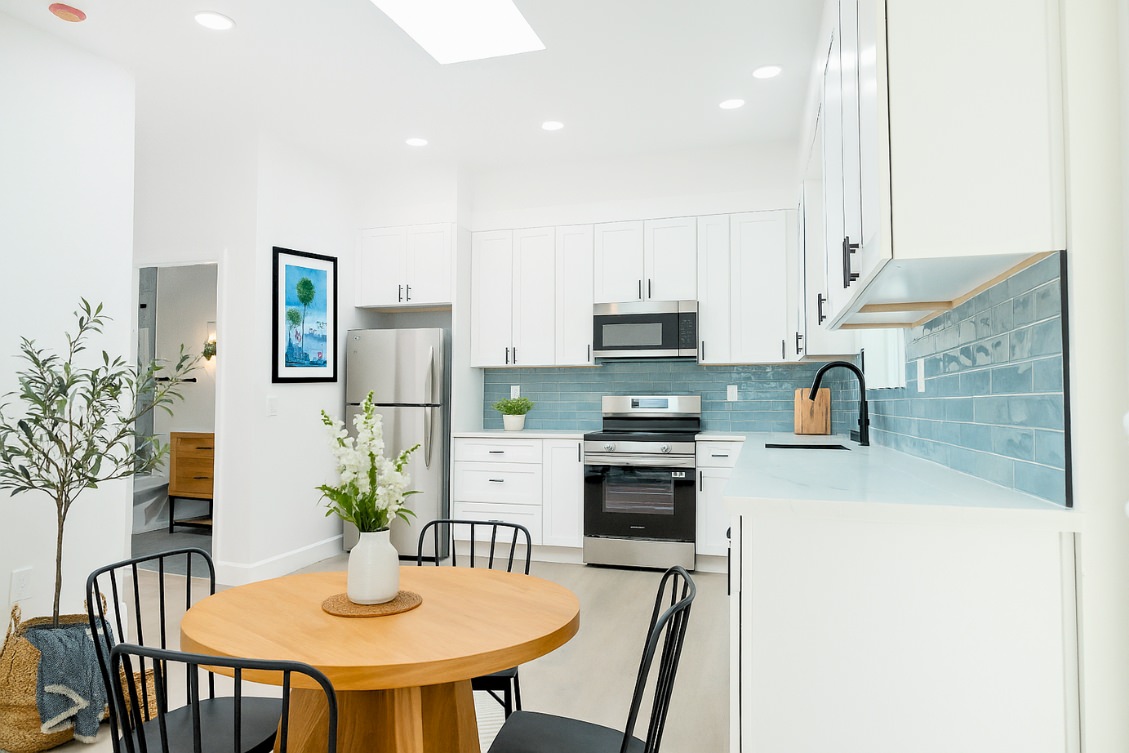 Open-concept ADU kitchen with white cabinets, blue backsplash, and round dining table