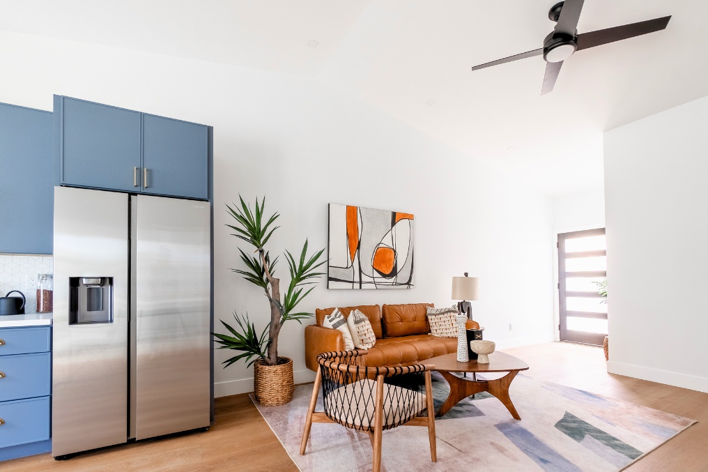 Modern ADU living room with brown leather sofa, abstract wall art, and blue kitchen cabinetry