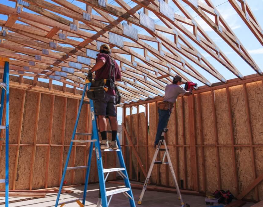 Two builders constructing an ADU wooden frame — What are the Different Types of ADUs illustration for California homeowners.