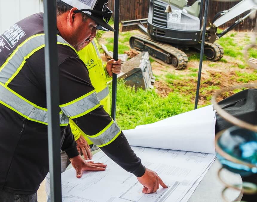 “Evaluating Existing Property Documentation” contractor reviewing large site plans outdoors, representing survey and record checks.