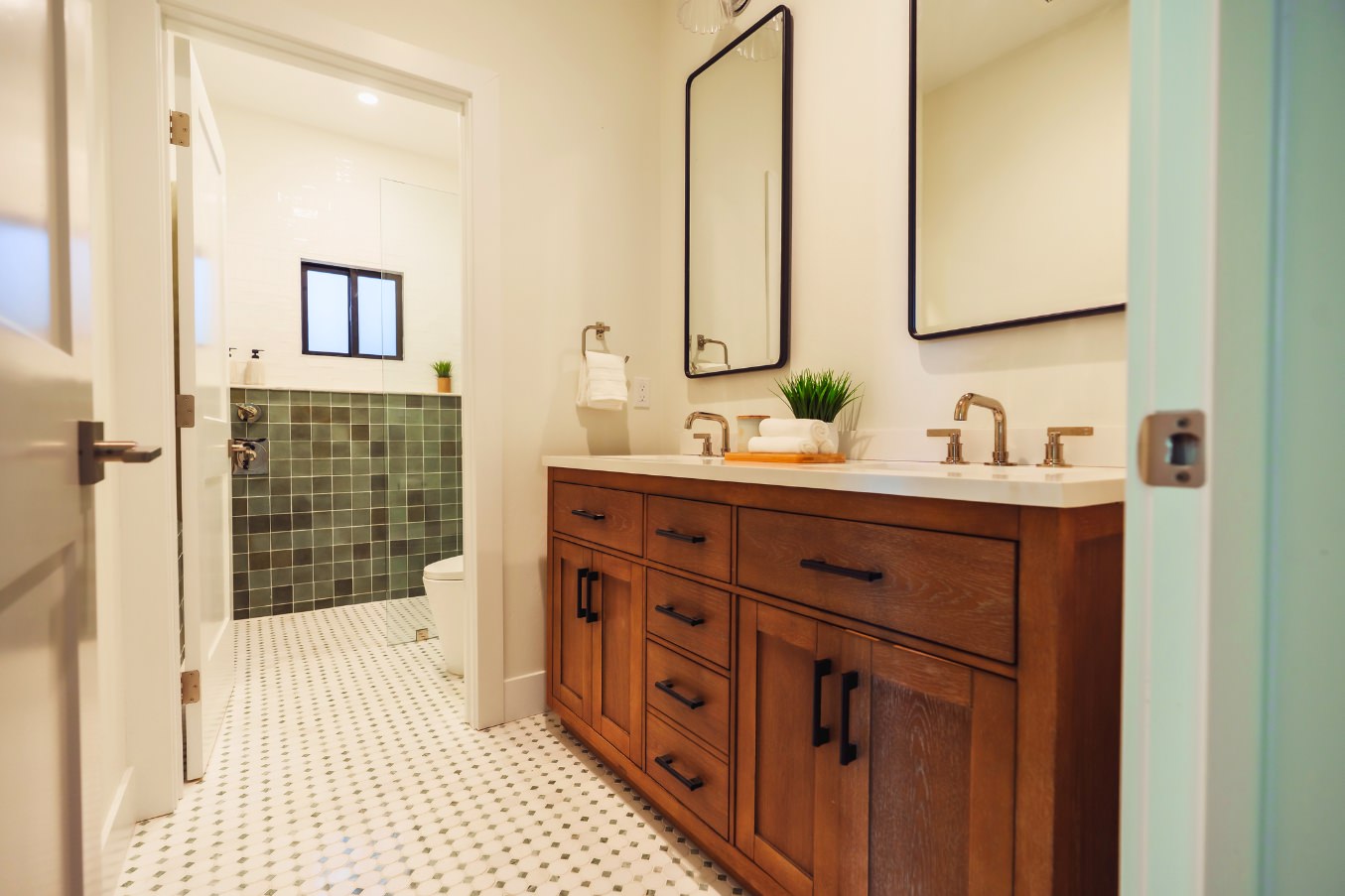 Bathroom in the Linda Vista Detached ADU showcasing a warm wood double vanity, dual mirrors, and patterned tile flooring leading into the shower area.