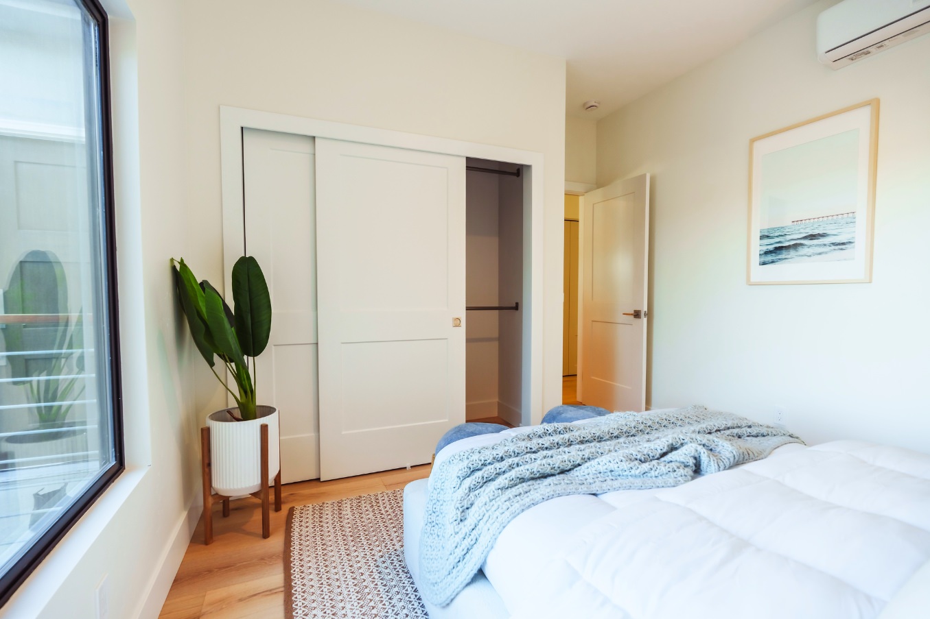 Bedroom inside the Linda Vista Detached ADU featuring sliding closet doors, a large window, a potted plant, and soft neutral decor.