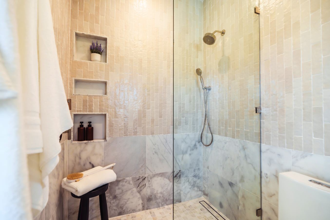 Shower in the Linda Vista Detached ADU with marble lower walls, vertical textured tile above, built-in niches, and a glass enclosure.